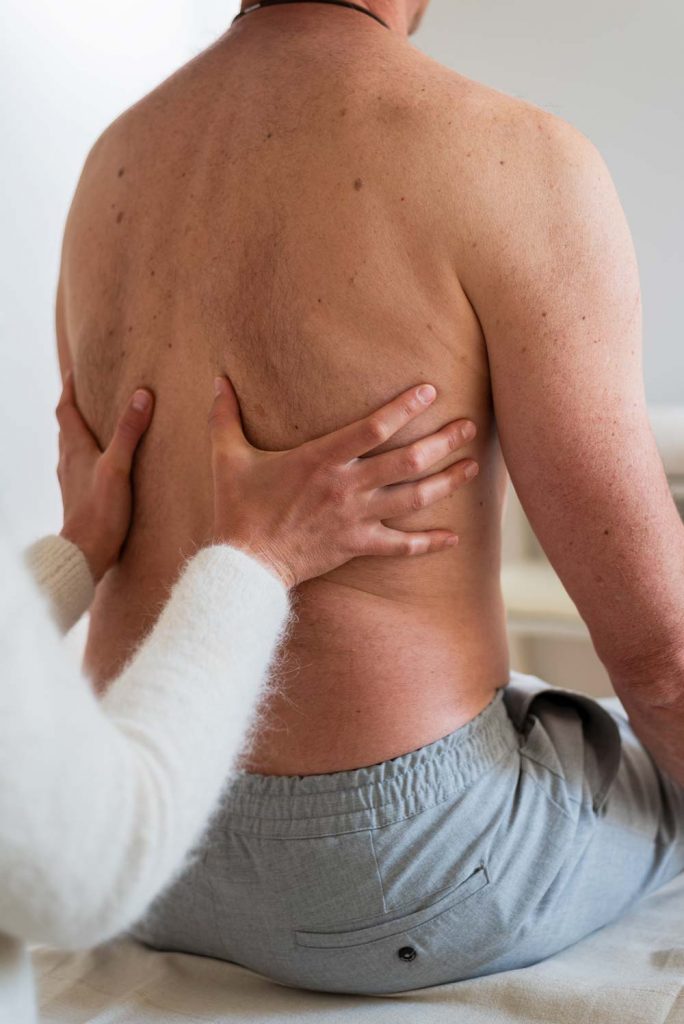 Physiotherapeutische Behandlung – Hände an einem Männerrücken für Mobilisation