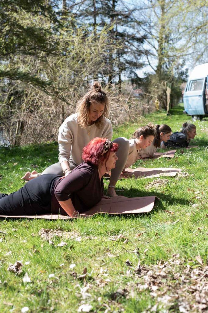 Christin Rupp Verbessert Haltung von ihrer Yoga-Teilnehmerin bei der Yogapose Cobra. Die Yogastunde findet draußen im Grünen statt.