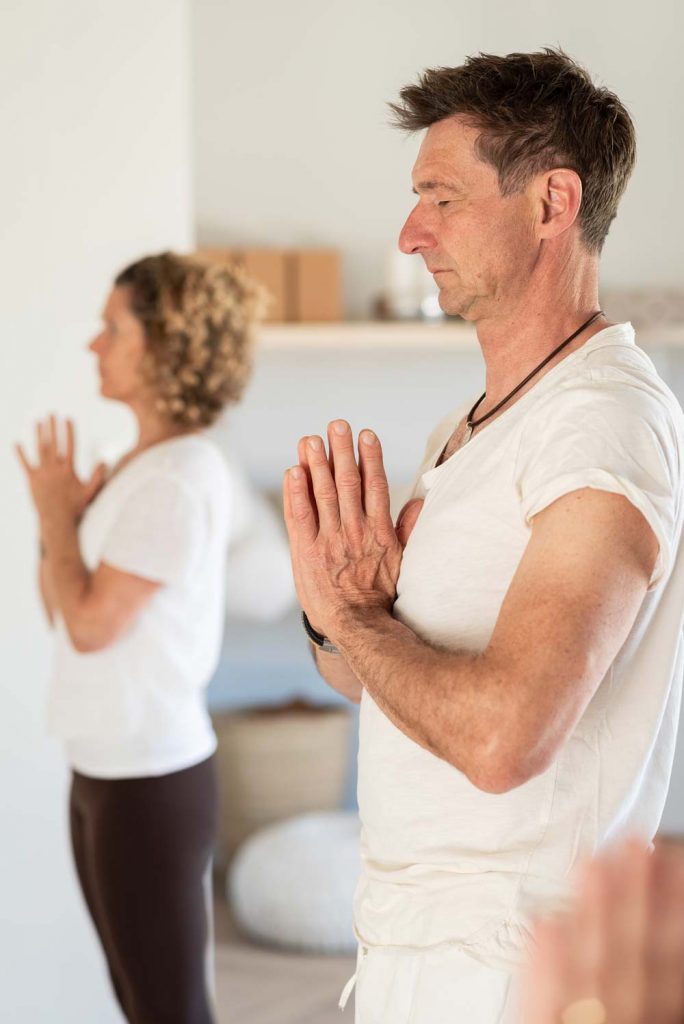 Ein Mann und eine Frau in hellen T-Shirts bei einer achtsamen Begrüßung mit Namasté-Geste