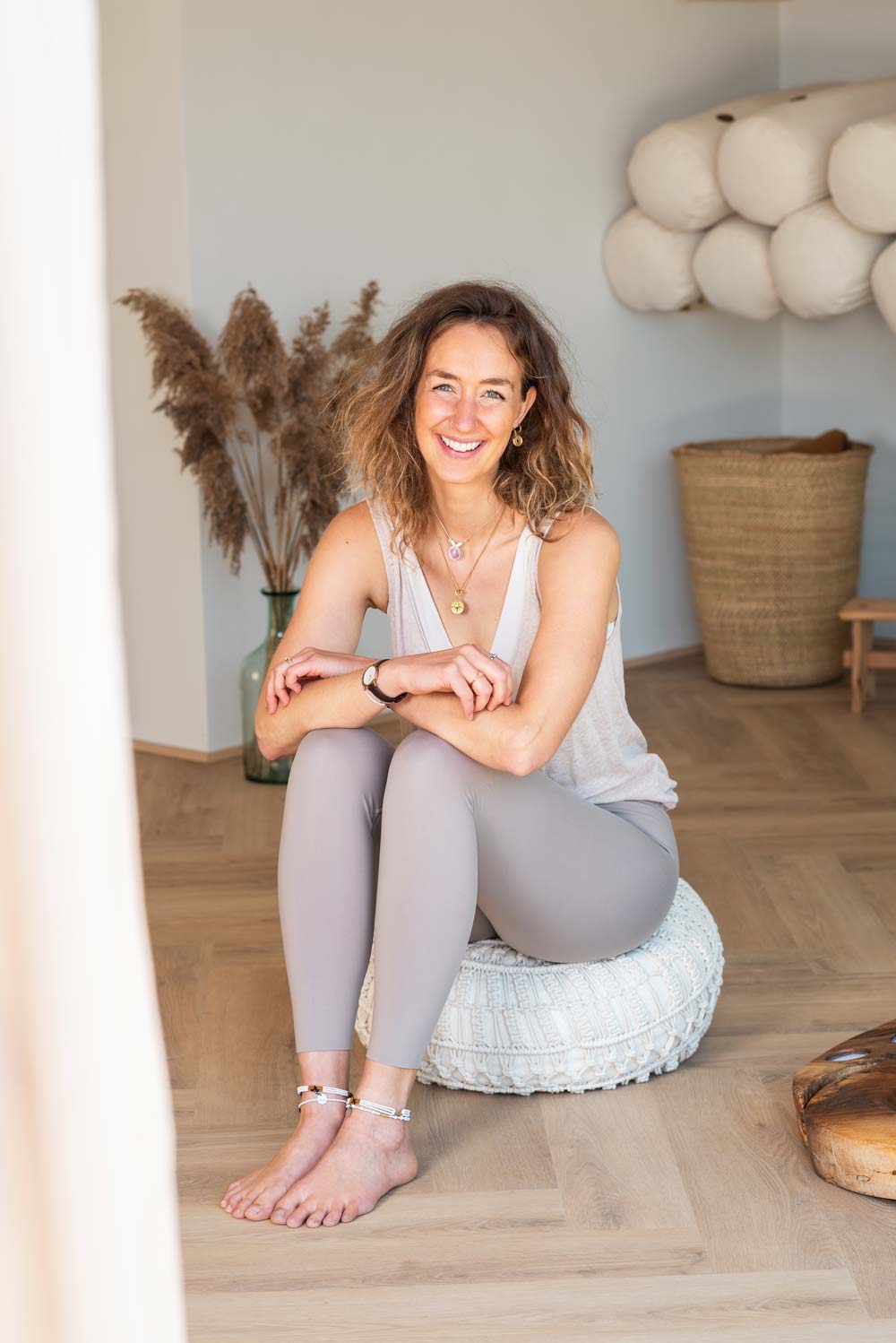 Christin Rupp sitzt lächelnd auf einem Meditationskissen im Yogabereich – entspannte Sitzhaltung, freundliche Begrüßung